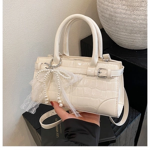 Détail du sac seau crème avec motif crocodile et breloque noeud en dentelle et perles