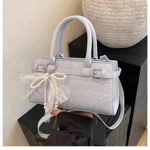 Détail du sac seau bleu clair à motif crocodile avec nœud en perles et décor en dentelle