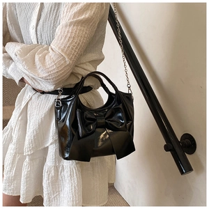 Detailaufnahme der schwarzen Lackleder-Beuteltasche mit großer Schleife und Metallkette
