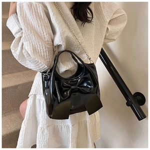 Detail einer schwarzen glänzenden Beuteltasche mit großer Schleife und silberner Kette