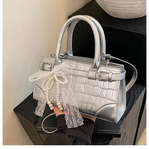 Détail du sac seau argenté à motif crocodile avec nœud en dentelle et perle