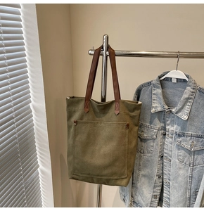 Detalle del bolso tote de lona verde militar con asas de cuero marrón y bolsillo