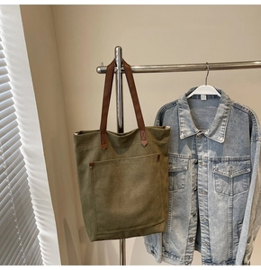 Detalle del bolso tote de lona verde militar con asas de cuero marrón y costuras reforzadas