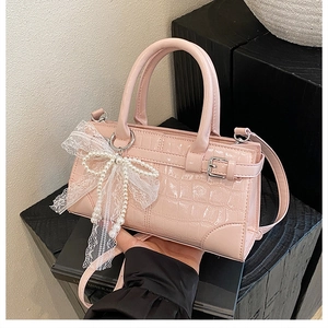Détail du sac seau rose effet crocodile avec nœud en dentelle et breloque en perle
