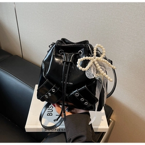 Détail du sac seau noir brillant avec fermeture à cordon et breloque nœud en perles