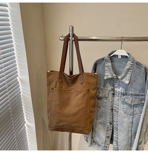 Detalle del bolso tote de lona marrón con remaches metálicos en el bolsillo frontal