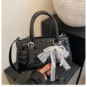 Détail du sac seau noir motif crocodile avec charm nœud en dentelle et perles