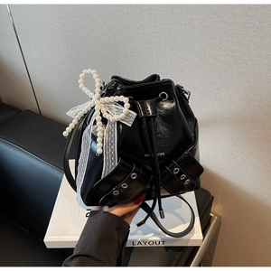 Détail du sac seau noir brillant avec rubans en dentelle et nœuds en perles larges