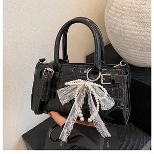 Détail d'un sac seau noir motif crocodile avec nœud perlé et boucles argentées