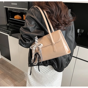Détail du sac à bandoulière beige avec foulard, breloque perle et texture gaufrée