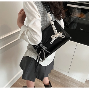 Detail of black leather shoulder bag with lace bow decoration and beaded charms