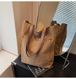 Detalle del bolso tote de lona marrón oscuro con asas de cuero y remaches metálicos