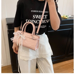 Détail du sac seau rose en cuir croco avec perles et nœud en dentelle blanche