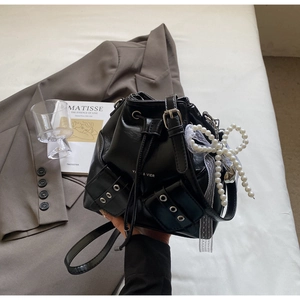 Détail d'un sac seau noir en similicuir avec poches et charm nœud en dentelle et perles