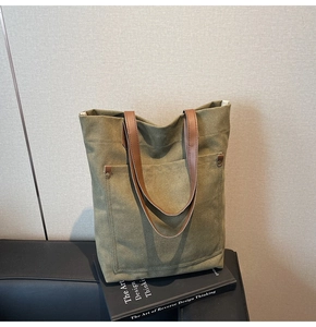 Detalle de bolso tote de lona verde oliva con asas de cuero y remaches de latón