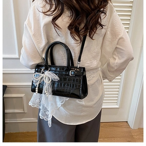 Détail du sac seau noir motif crocodile avec nœud en dentelle et perle sur un mannequin