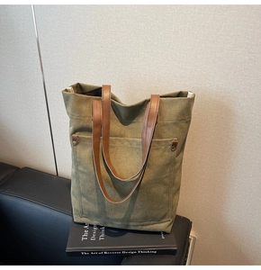Detalle de bolso tote de lona verde militar con asas de piel sintética marrón y bolsillo remachado
