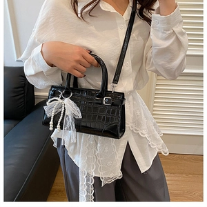 Détail du sac seau noir motif crocodile avec nœud en dentelle blanche et perle