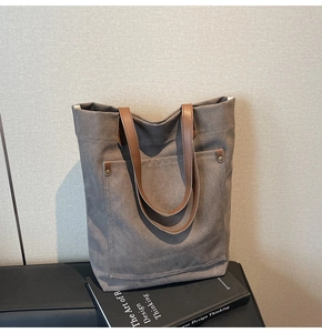 Detalle de bolso tote de lona gris con asas de cuero marrón y remaches de metal fino
