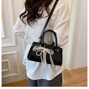 Détail du sac seau noir motif crocodile avec nœud en dentelle blanche et breloque perle