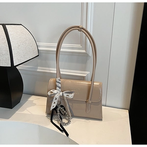 Close-up of beige glossy leather handbag with ribbon bow and metal bead charms