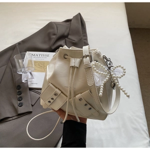 Détail du sac seau crème avec pendentif nœud en perles et poches de style industriel