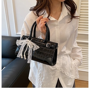 Détail du sac noir motif crocodile avec nœud en dentelle blanche et perles