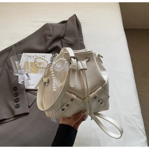 Détail d'un sac seau blanc crème avec breloque nœud perlé et cordon sur costume marron