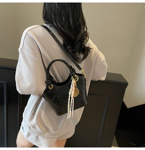 Detail of black leather bucket bag with embossed rabbit pattern and decorative leaf charm