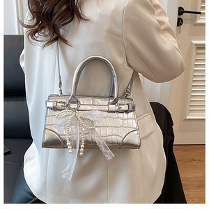Détail du sac seau argenté à motif crocodile avec nœud en dentelle et perles