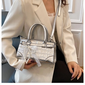 Détail d'un sac argenté à texture croco avec perle et nœud en dentelle sur mannequin