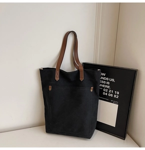 Detalle de bolso tote de lona negra minimalista con asas de cuero y remaches metálicos