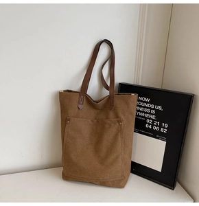 Detalle de bolso tote de lona marrón con bolsillo frontal, remaches y asas de cuero