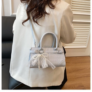 Sac seau bleu à motif crocodile avec charm nœud en perles porté par mannequin