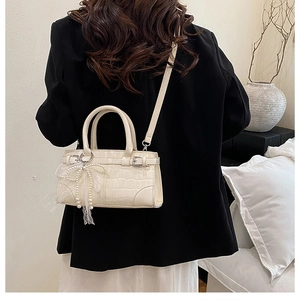 Détail du sac seau crème à texture crocodile brillante et pendentif nœud perlé