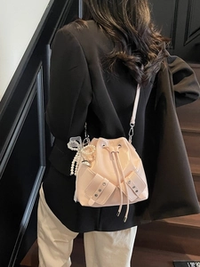 Sac seau en cuir verni brillant rose avec nœud perlé et dentelle porté par un mannequin