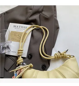 Detail of yellow crescent bag with rope knot handle and pearl charm on a grey blazer
