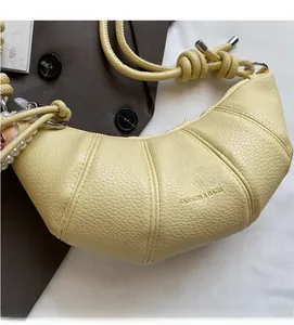 Detail of lychee textured croissant bag with woven strap and pearl charm accent