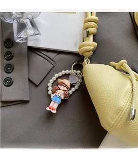 Detail of yellow lychee leather bag with pearl charm and cute cartoon girl keychain