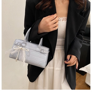 Détail du sac seau bleu clair à motif crocodile avec nœud en perles et dentelle