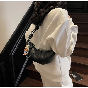 Detail of black crescent bag featuring knotted straps and a pearl girl charm accessory