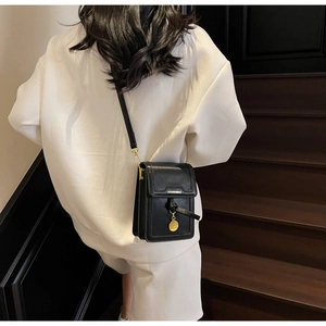 Detail of black leather crossbody phone bag with gold metal charm on model's back