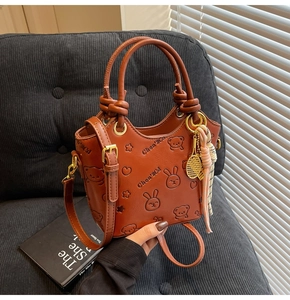 Detail of embossed brown leather bucket bag with cute bear patterns and tennis charm