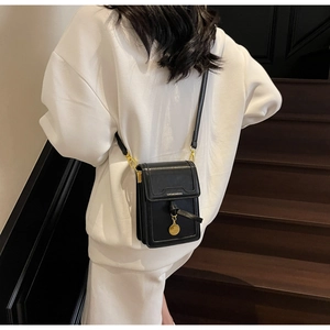 Detail of minimalist black leather crossbody phone bag with gold metal pendant on model