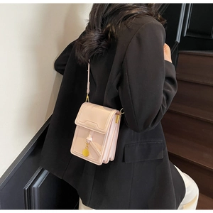 Side view of a nude pink leather crossbody bag with a gold ring charm and accordion style
