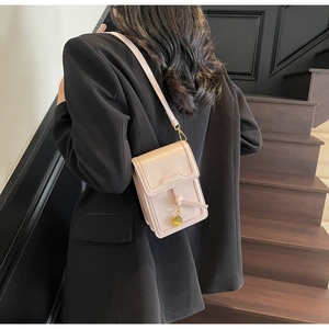Detail of light pink mini crossbody bag with gold hardware worn over a black blazer