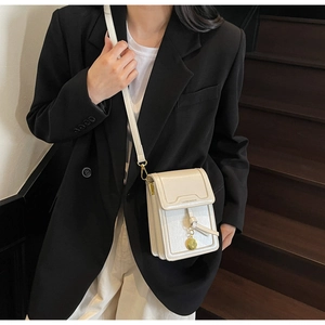 Detail of off-white crossbody phone bag with gold charm on a stylish model