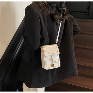 Detail view of white mini crossbody phone bag with knot decor and golden charm on model