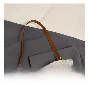 Detail showing beige woven straw bag with dark brown leather handle and white lace bow