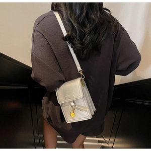 Detail of silver-grey crossbody phone bag with gold hardware and knot decor on stairs
